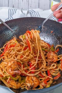 spaghetti with seared shrimp, bell peppers and onions dressed in creole sauce in a wok.